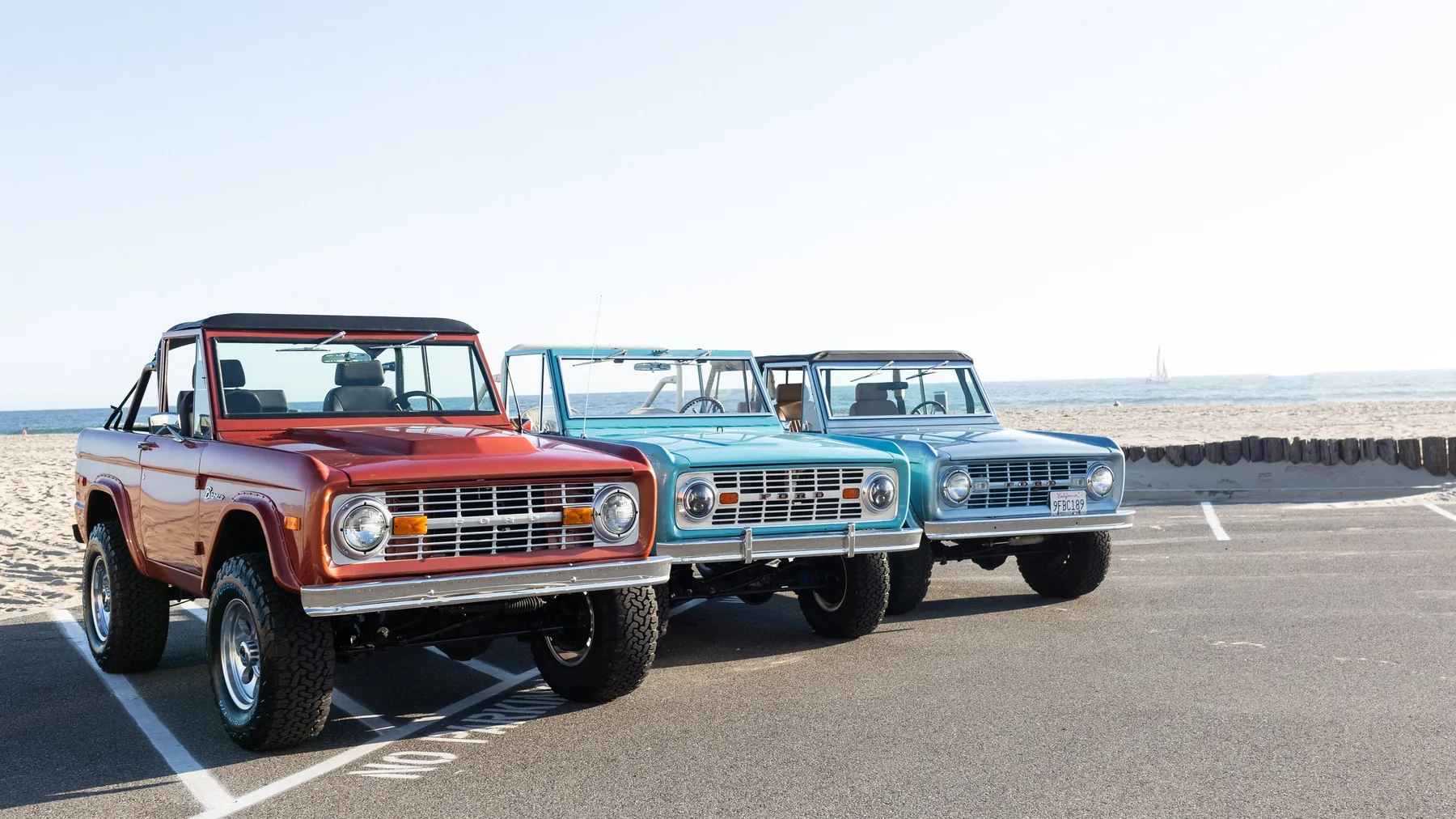 Three restored early Ford Broncos parked at the edge of Venice Beach at golden hour