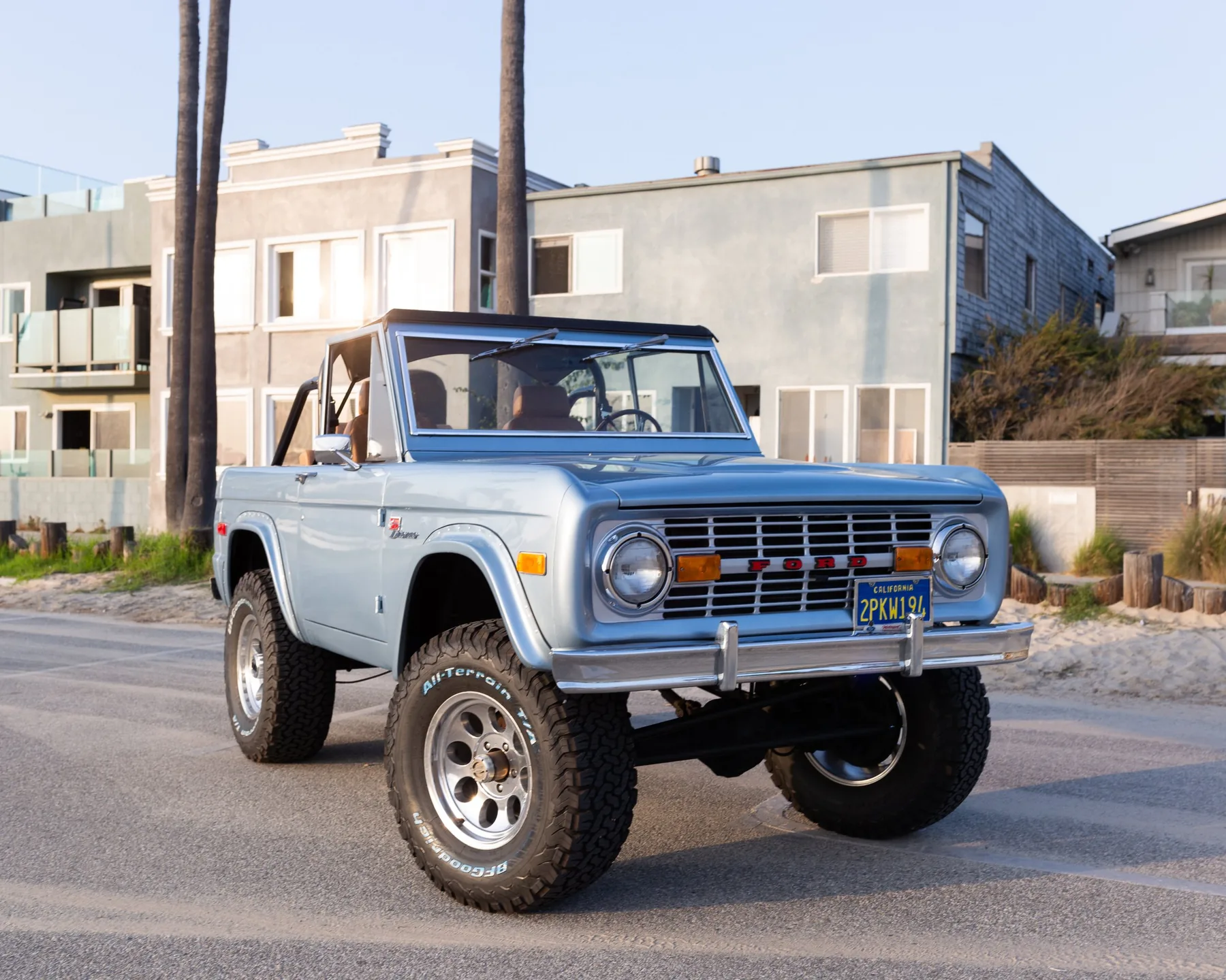 A pale blue early Bronco with saddle leather interior parked on a Venice walk street